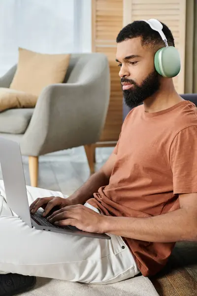 A relaxed man engages with his laptop while wearing headphones at home. — Stock Photo