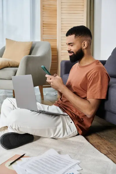 A relaxed man interacts with his phone and laptop on the floor. — Stock Photo