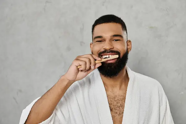 Um homem escova os dentes, sorrindo em um manto macio em casa. — Fotografia de Stock