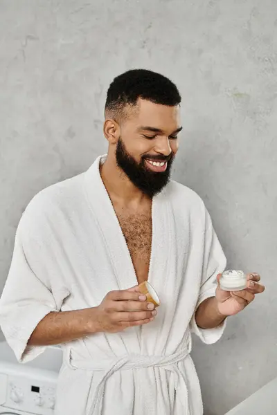 Man smiles while applying skincare in a minimalist bathroom setting. — Stock Photo