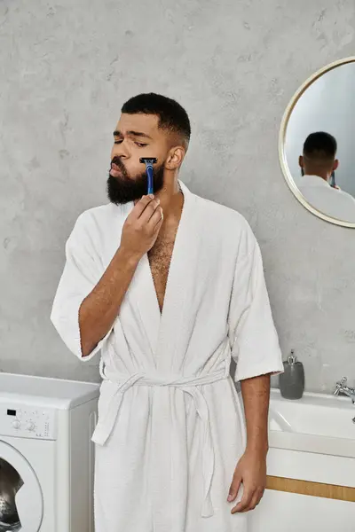 A man in a robe shaves while enjoying a tranquil morning at home. — Stock Photo