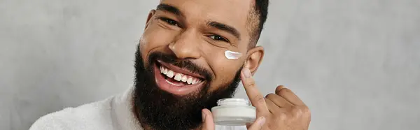L'homme applique de la crème sur son visage, mettant en valeur un moment joyeux de soins de la peau à la maison. — Photo de stock