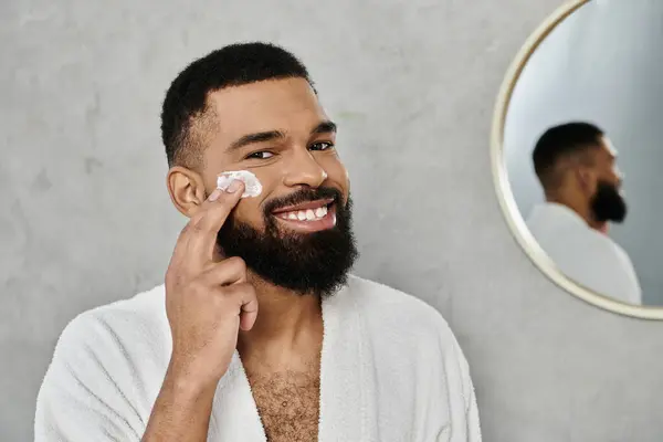 A man applies skincare while smiling in a bright, modern bathroom. — Stock Photo