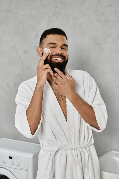 Um homem sorri enquanto aplica cuidados com a pele em casa, abraçando um momento de autocuidado e relaxamento. — Fotografia de Stock