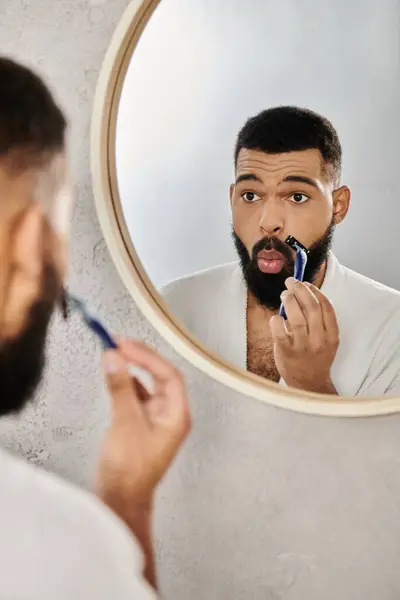 A man focuses on grooming while standing in front of a round mirror. — Stock Photo