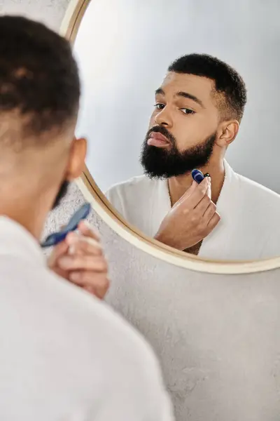 A man carefully grooms his beard in a serene bathroom setting. — Stock Photo