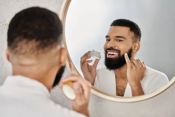 Man applies skincare in the mirror, smiling during his morning grooming ritual. — Stock Photo