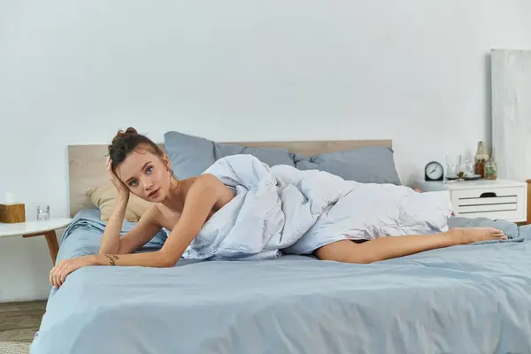A young woman lounges comfortably in playful lingerie amidst soft bedding. — Stock Photo