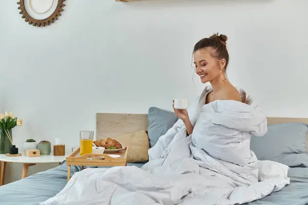 A young woman wrapped in blankets relishes a warm drink in cozy comfort. — Stock Photo