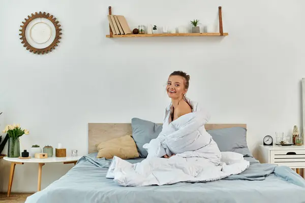 A cheerful young woman playfully enjoys the soft bedding in a bright, inviting room. — Stock Photo