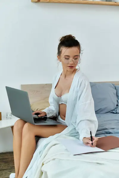 A stylish young woman writes notes while using her laptop in a serene bedroom. — Stock Photo