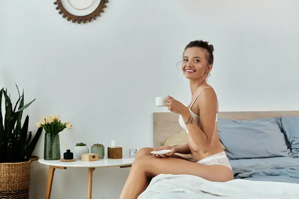 A young woman enjoys her coffee while seated on a stylish bed. — Stock Photo