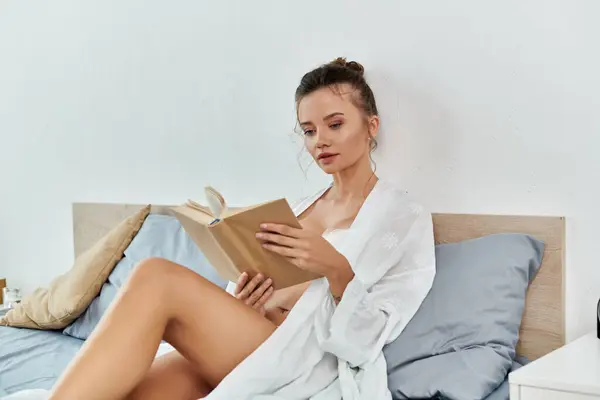 Uma jovem mulher gosta de ler em lingerie elegante, imersa em um livro em sua cama. — Fotografia de Stock