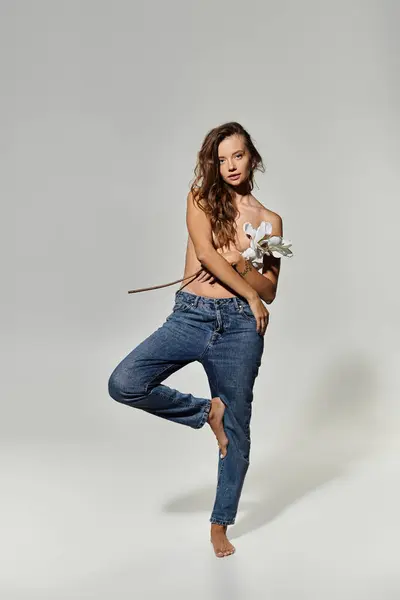 A young woman stands gracefully, holding a flower in her hand. — Stock Photo