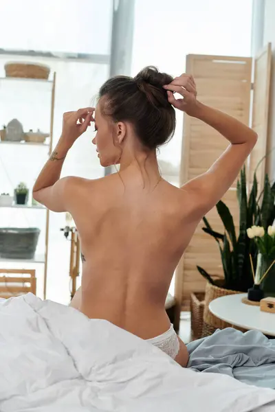 A young woman elegantly adjusts her hair in a cozy, stylish bedroom. — Stock Photo