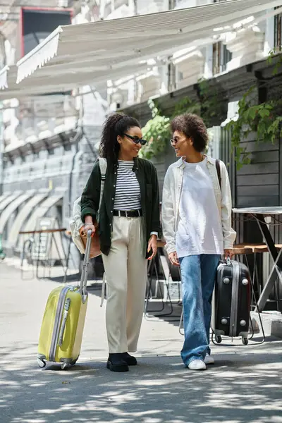 A happy couple strolls through a European city, ready for adventure with their suitcases in tow. — Stock Photo