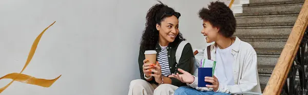 A joyful lesbian couple relaxes near stairs, sharing laughter and drinks while exploring together. — Stock Photo