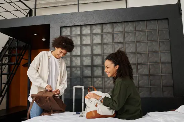 Two joyful women share laughter and stories while unpacking their bags in a cozy hotel room. — Stock Photo