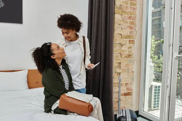 Two happy women share laughter and love in their cozy hotel room while exploring their destination. — Stock Photo