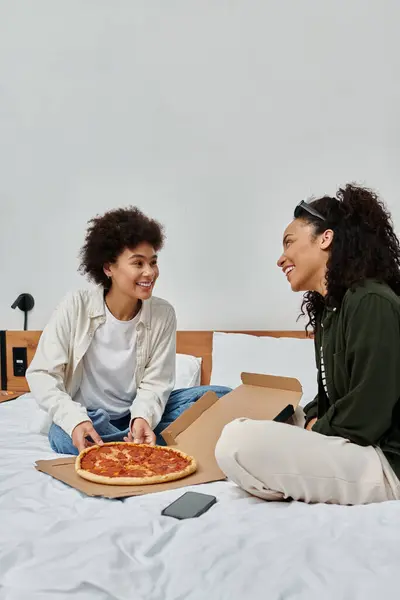 A happy couple shares laughs and delicious pizza while relaxing in their hotel room. — Stock Photo