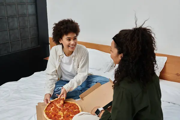 A cheerful couple shares a pizza and laughter, creating cozy memories in their hotel room. — Stock Photo