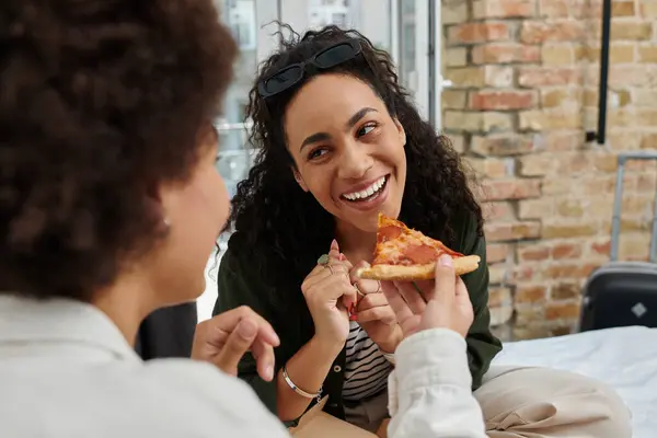 Two women share laughter and pizza in a warm hotel room, celebrating their time together. — Stock Photo