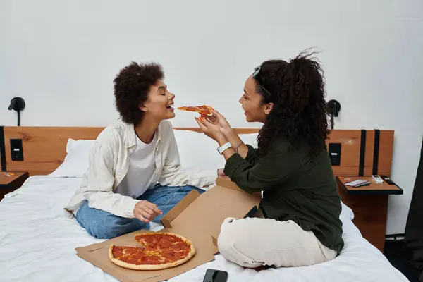 Um casal alegre compartilha uma fatia de pizza em seu quarto de hotel, celebrando amor e união. — Fotografia de Stock