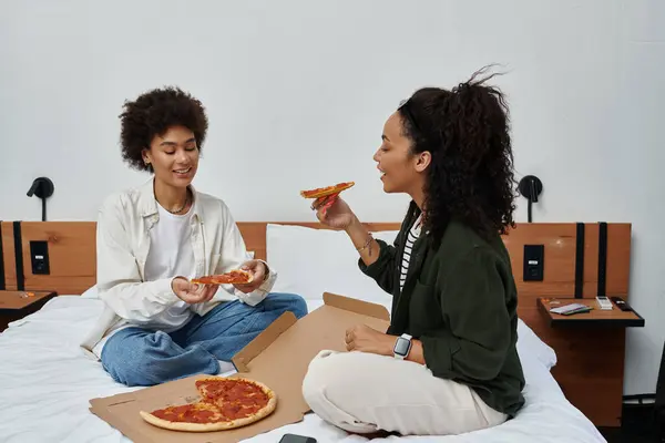 Two happy women share pizza and laughter in their hotel room, creating cherished memories together. — Stock Photo