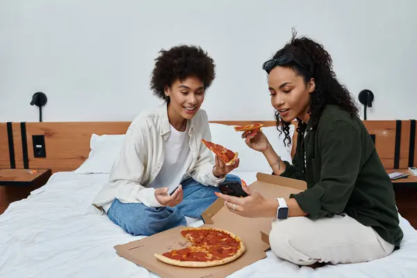 Zwei Frauen teilen Lachen und Pizza in ihrem gemütlichen Hotelzimmer und fangen Momente der Liebe und des Abenteuers ein. — Stock Photo