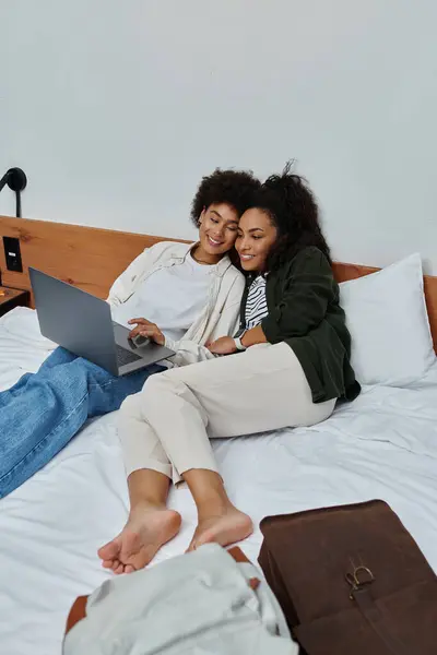 A happy couple relaxes together on a hotel bed, sharing laughter while watching something on a laptop. — Stock Photo