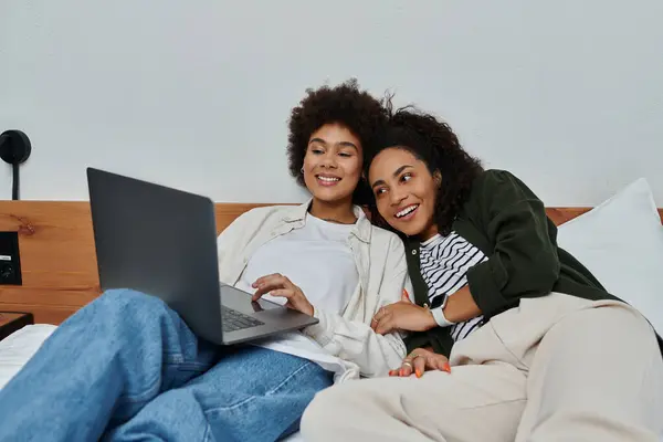 Two happy women relax together in their hotel room, sharing laughter and moments while watching a laptop. — Stock Photo