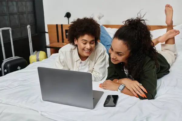 Two women share laughter and connection while exploring online together in their hotel room. — Stock Photo