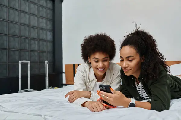 Duas mulheres compartilham risos e momentos de alegria enquanto relaxam em seu acolhedor quarto de hotel. — Fotografia de Stock