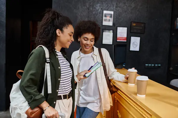 Ein fröhliches Paar checkt begeistert an der Rezeption eines lebhaften Hostels ein und nippt gemeinsam am Kaffee.. — Stockfoto