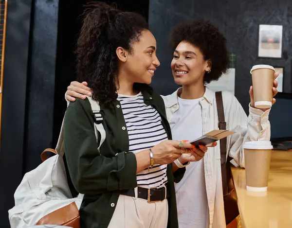 A joyful couple engages as they check in at a lively hostel reception, coffee cups in hand. — Stock Photo