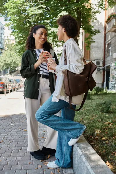 Two joyful women share coffee and laughter while exploring the vibrant city outdoors. — Stock Photo