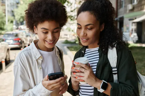 A joyful African American lesbian couple shares a moment together, sipping coffee and chatting outdoors. — Stock Photo