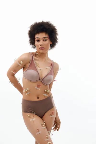 Bella donna afroamericana con i capelli ricci in posa con fiori sul corpo e biancheria intima. — Foto stock