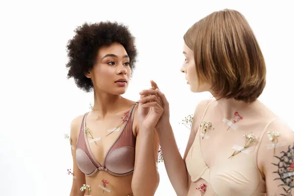 Two women share a tender gaze, decorated with delicate floral accents on their skin. — Stock Photo