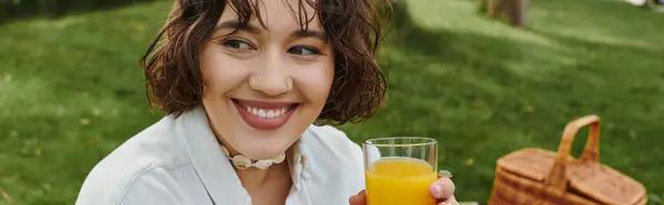 Une jeune femme joyeuse se détend en été, sirotant une boisson rafraîchissante au milieu d'un cadre de pique-nique pittoresque. — Photo de stock