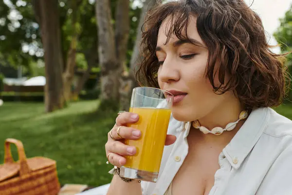 Relaxing under the summer sun, a young woman sips a refreshing drink amidst a delightful picnic. — Stock Photo