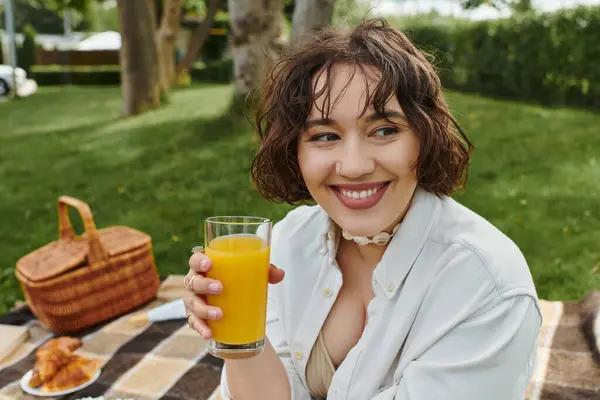 A young woman enjoys a sunny picnic break, savoring a refreshing drink amid nature beauty. — Stock Photo