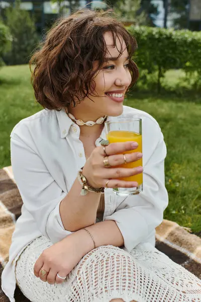 Una hermosa joven se relaja en un picnic de verano, tomando una bebida fresca y disfrutando del clima soleado. - foto de stock