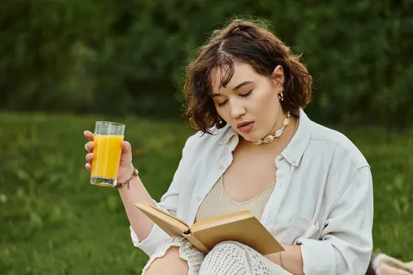 A pretty young woman relaxes in a summer picnic, savoring a book and refreshing drink amidst nature. — Stock Photo
