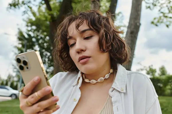A pretty young woman relaxes in summer, wearing a white shirt and using her phone. — Stock Photo