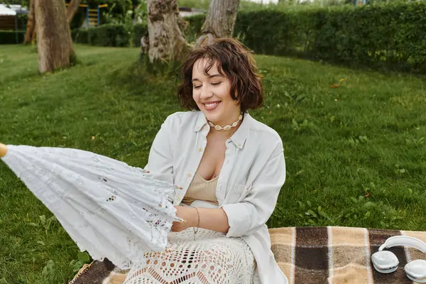 Uma mulher alegre em uma camisa branca se deleita em um piquenique de verão, desfrutando de um céu quente com um guarda-sol encantador.. — Fotografia de Stock