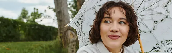 A cheerful young woman relaxes in summer, savoring a picnic while sheltered under a lace umbrella. — Stock Photo