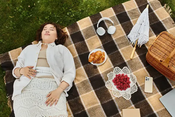 A young woman enjoys a peaceful summer picnic, surrounded by delicious snacks and warm sunshine. — Stock Photo