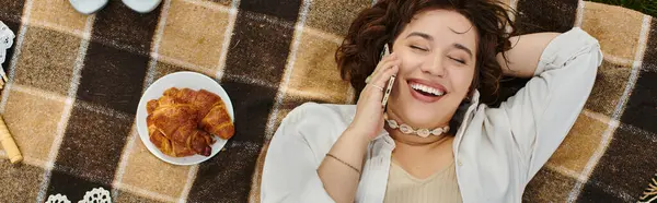 Una giovane donna si rilassa su una coperta da picnic, sorridendo gioiosamente mentre si gode una giornata estiva soleggiata all'aperto. — Foto stock