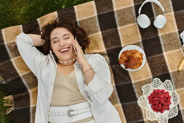 A joyful woman relaxes on a blanket, savoring treats and the beauty of summer sunshine. — Stock Photo